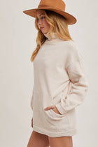 Woman wearing a beige sweater dress and brown hat on a white background