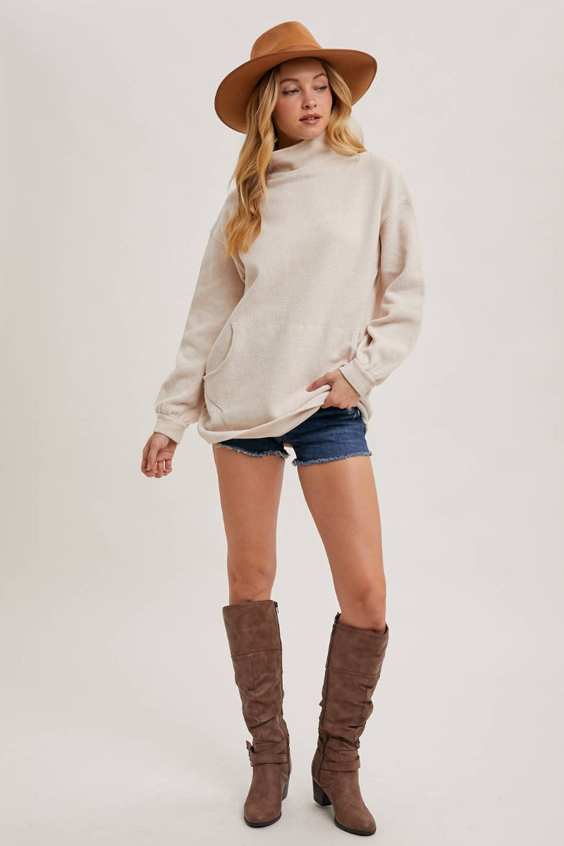 Woman wearing a beige sweater, denim shorts, and brown knee-high boots on a white background