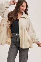 Woman wearing a beige jacket, black top, and gray jeans on a white background