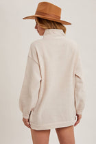 Person wearing a beige sweater and brown hat on a plain background