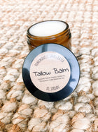 Jar of tallow balm with a black lid on a textured beige surface