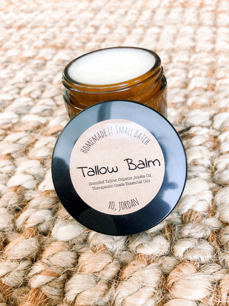 Jar of tallow balm with a black lid on a textured beige surface