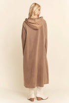 Woman wearing a long beige hoodie against a plain background