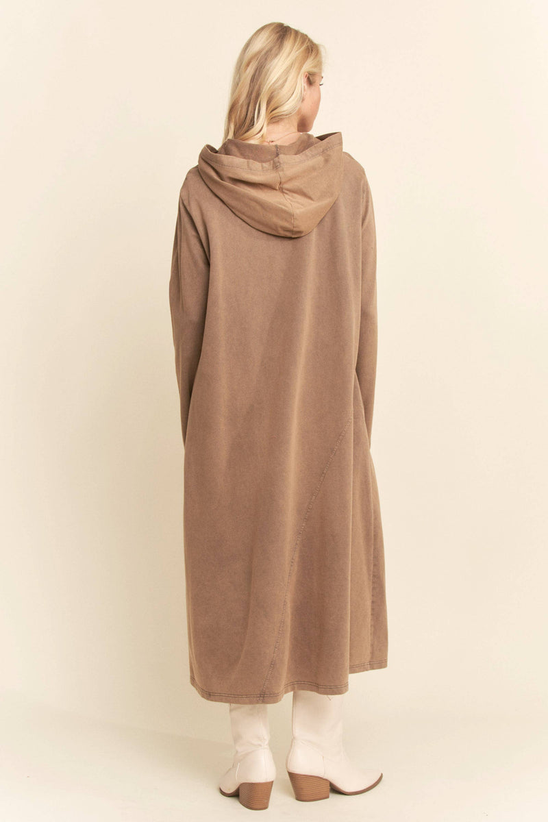 Woman wearing a long beige hoodie against a plain background