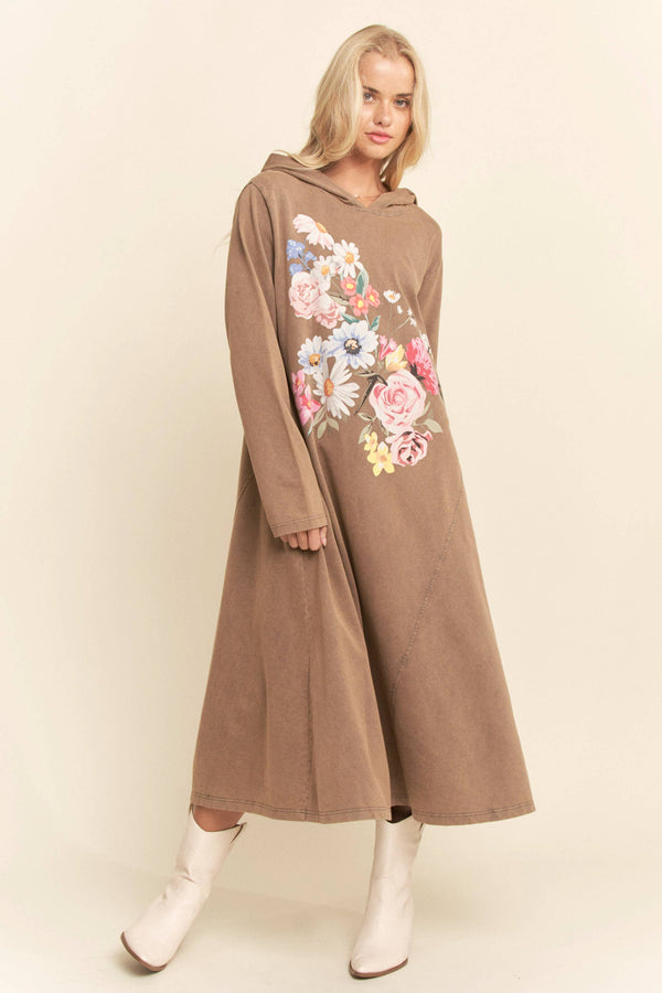Woman wearing a long brown dress with floral embroidery on a beige background