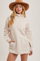 Woman wearing a beige sweater dress and brown hat on a white background